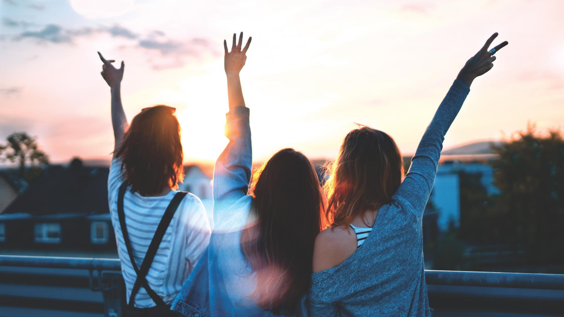 Drei junge Frauen recken die Hände in die Abendsonne