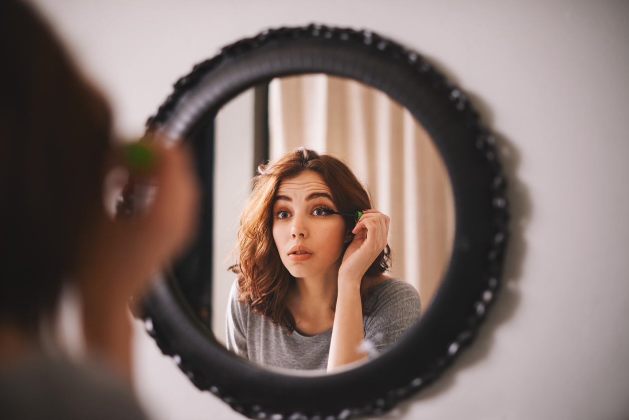 Frau trägt Make Up vor dem Spiegel auf