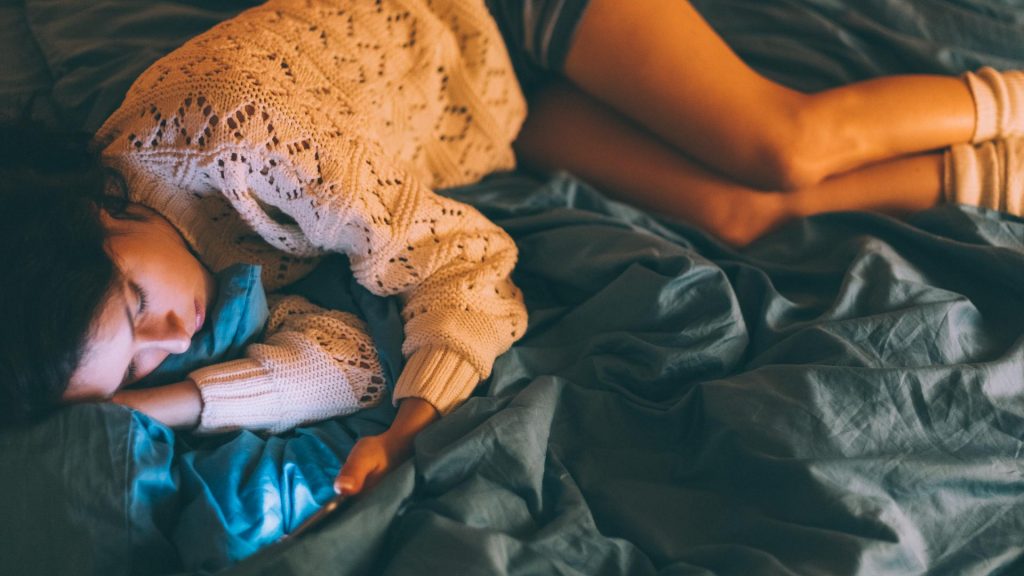 Frau liegt im Bett mit Handy