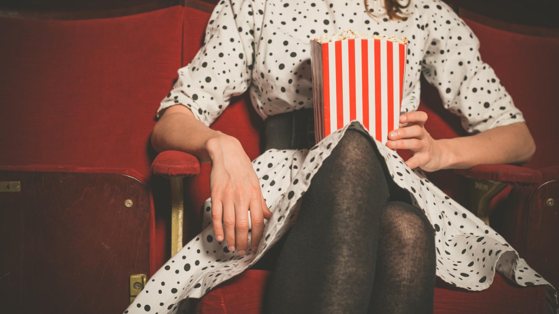 Frau sitzt mit Popcorn in der Hand im Kinosaal