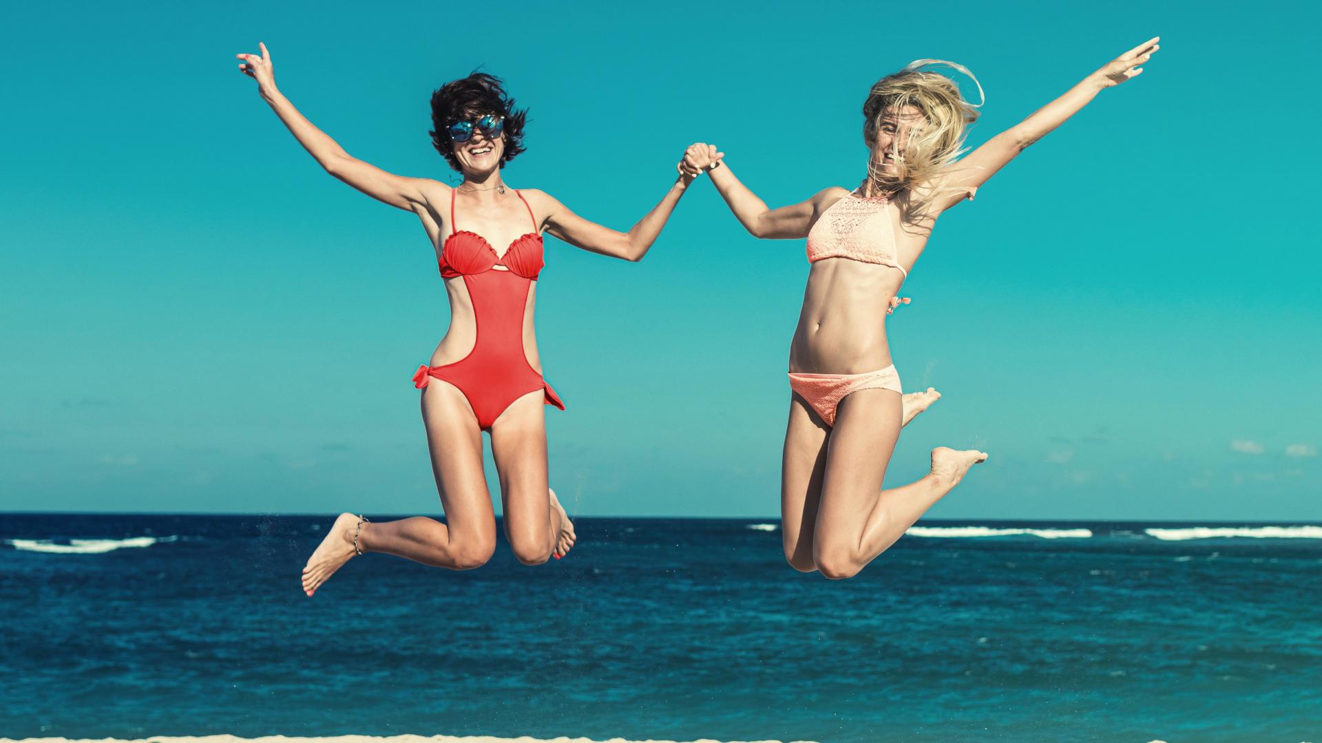 Zwei Freundinnen springen vergnügt hoch am Strand