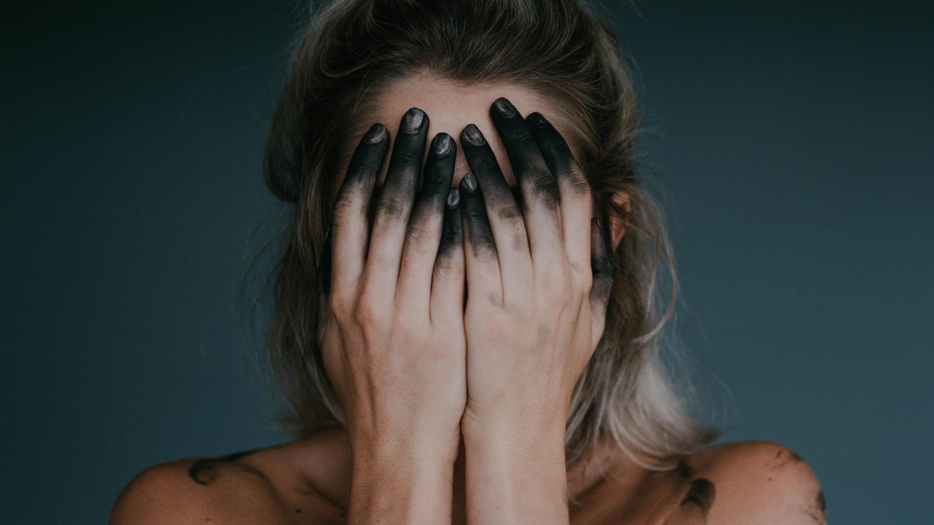 Frau mit schwarz gefärbten Fingern hält sich die Hände vor das Gesicht
