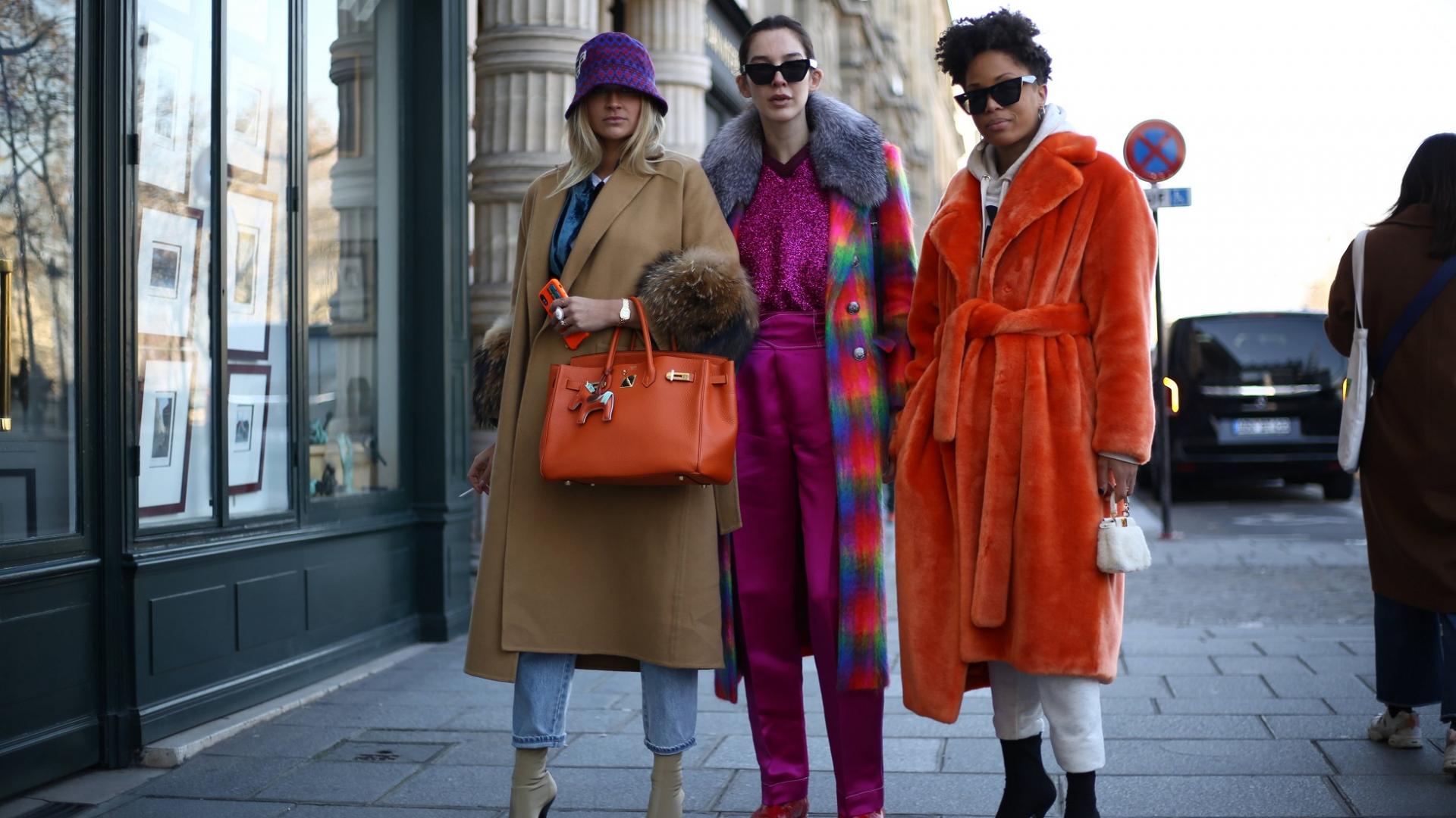 drei Frauen auf dem Bürgersteig mit modischer Kleidung und orangfarbener Hermès Tasche
