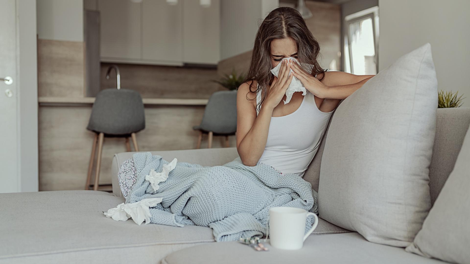 Kranke, erkältete Frau eingewickelt in einer Decke auf der Couch mit benutzten Taschentüchern