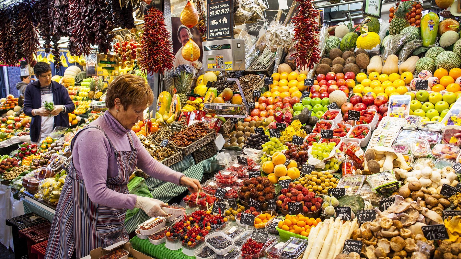 ältere Verkäuferin steht auf dem Wochenmarkt und verkauft Obst & Gemüse
