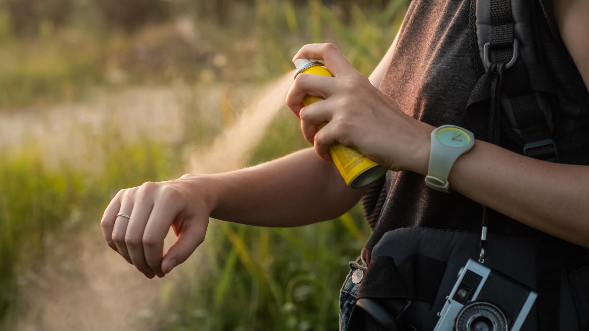 Frau sprüht sich Mückenspray auf den Arm