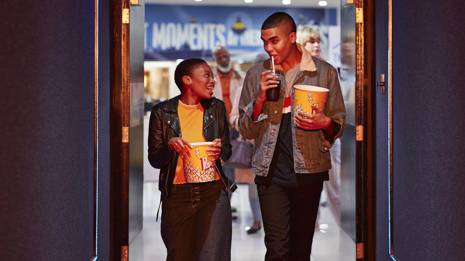 Happy young friends talking while walking in corridor at movie theater