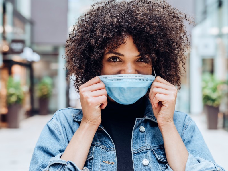 frau afro haare maske jeansjacke lächeln