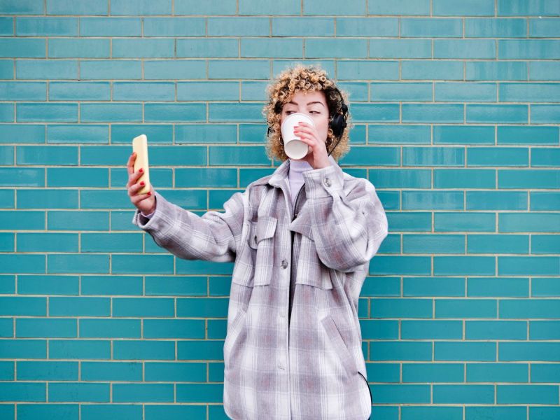 Frau mit Kaffeebecher vor blauer Wand