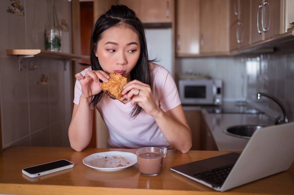 Frau isst vor dem Laptop