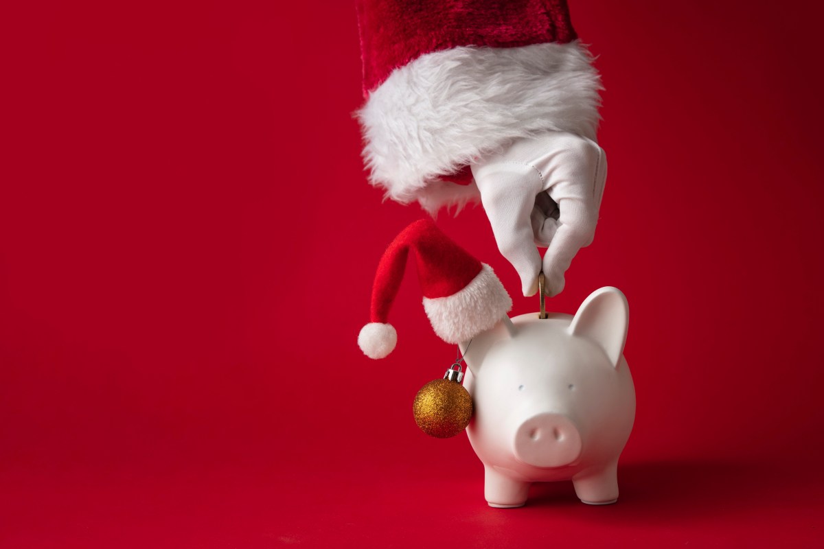 Eine Hand schmeißt Geld in ein Sparschwein mit Weihnachtsmütze.