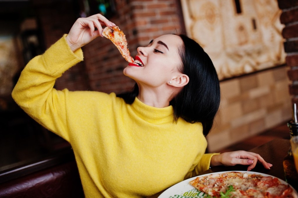 Frau im gelben Pullover isst Pizza