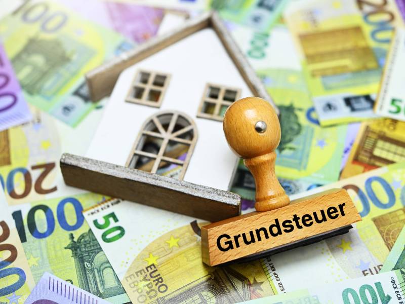 Haus und ein Stempel mit der Aufschrift "Grundsteuer" liegt auf Euro-Geldscheinen.