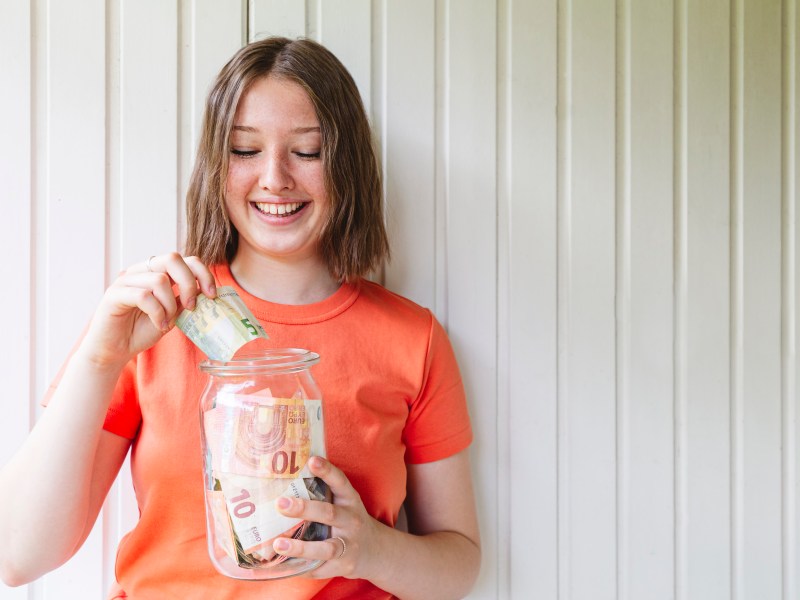 Junge Frau hält ein Glas mit Bargeld in der Hand.