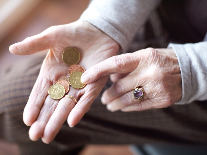 In der Hand einer Seniorin liegen mehrere Münzen.