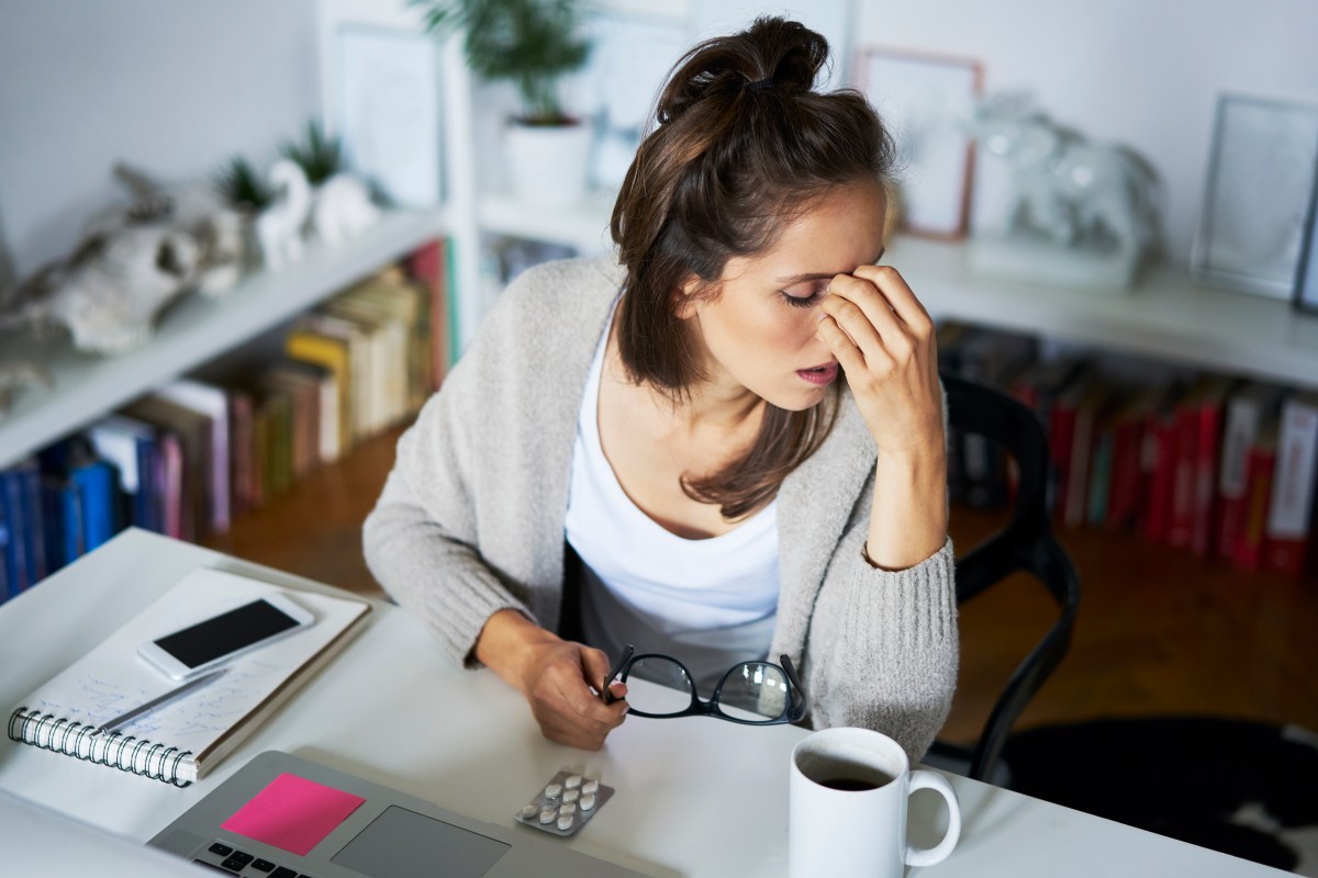 Junge Frau sitzt sehr erschöpft am Arbeitsplatz