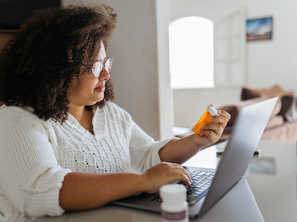 Frau sitzt mit Medikamenten am Laptop.