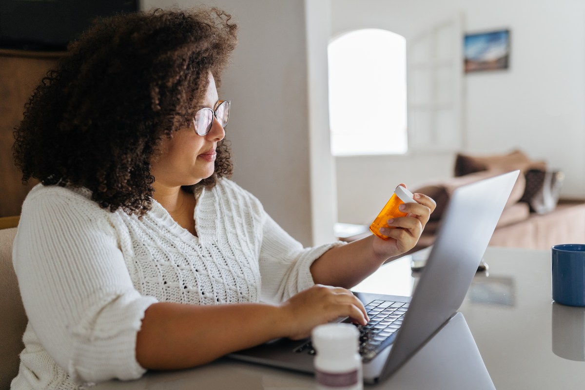 Frau sitzt mit Medikamenten am Laptop.