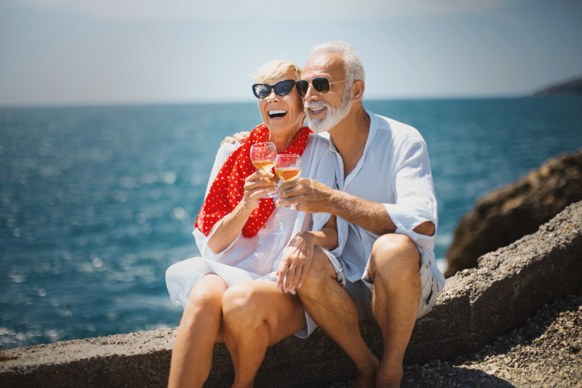 Ein RentnerpÃ¤rchen sitzt am Meer und trinkt Wein.