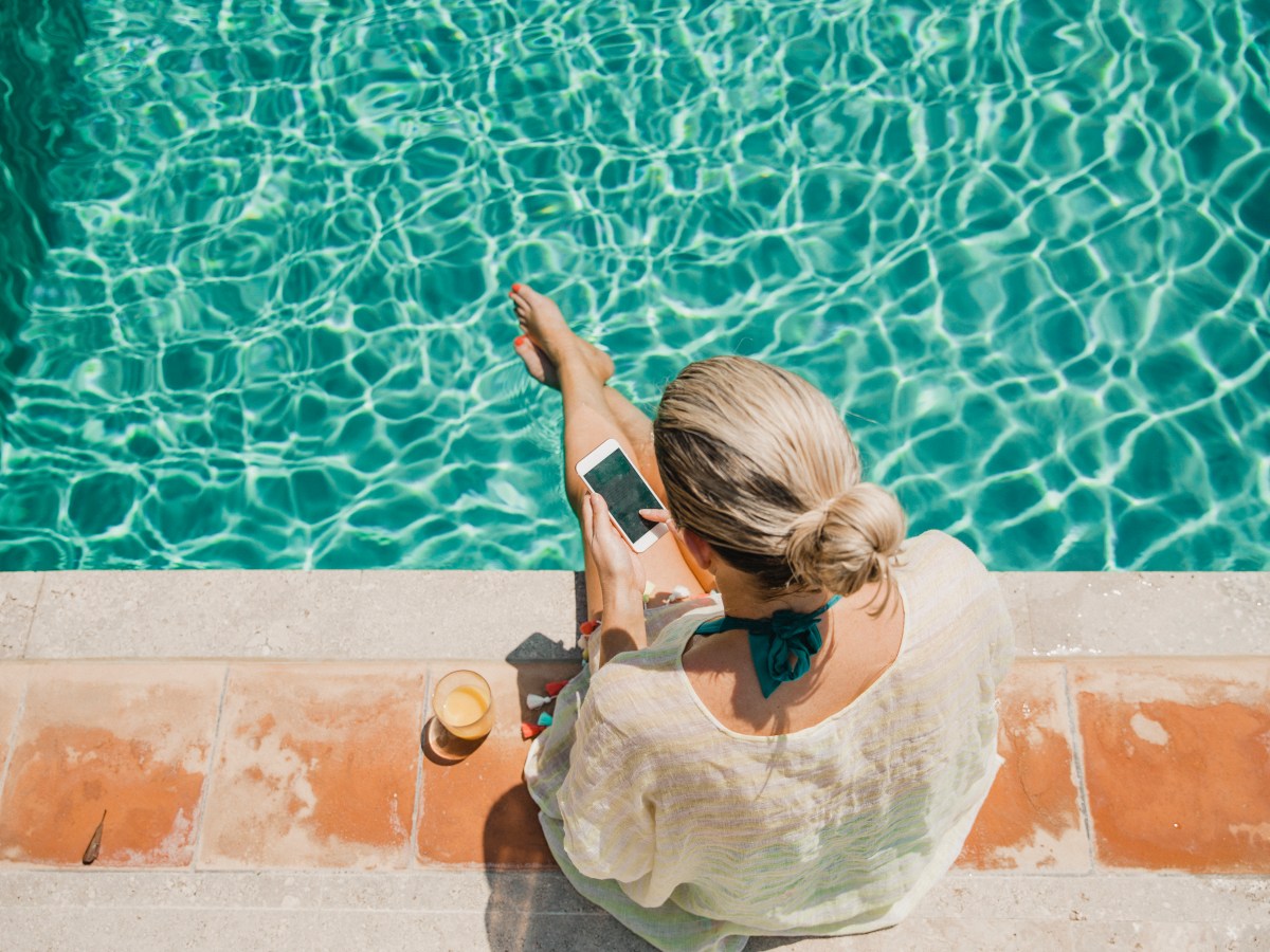 Eine Frau sitzt mit Handy am Pool.