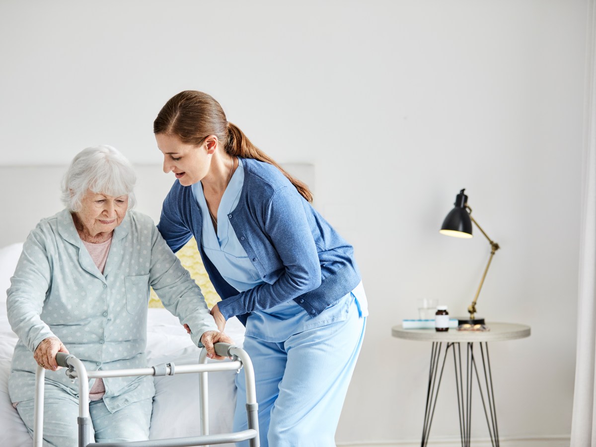 Pflegekraft hilft einer Ã¤lteren Frau beim Aufstehen.