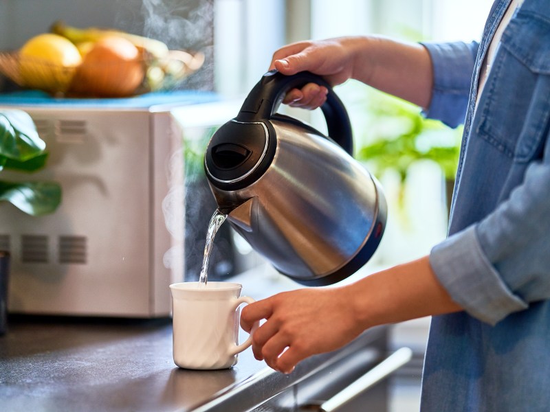 Person schüttet sich warmes Wasser in die Tasse.