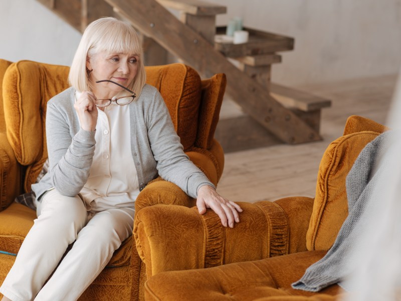 Eine Seniorin sitzt in ihrem Sessel und schaut auf einen leeren Platz.