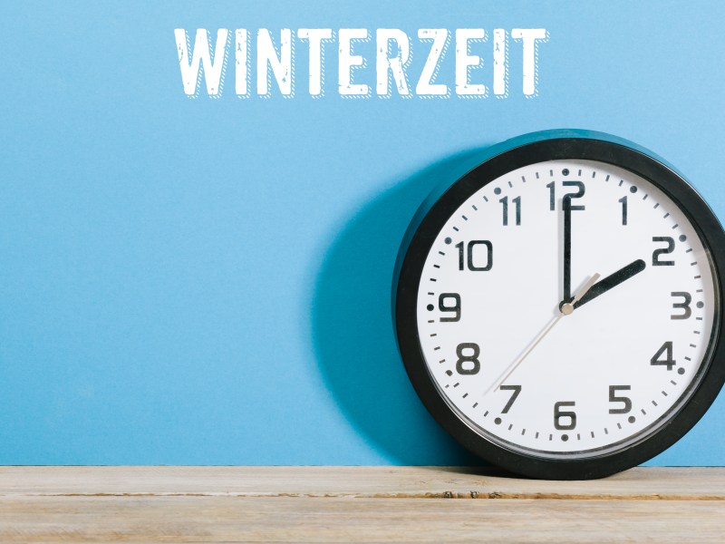 Eine Uhr steht auf einem Tisch. Ãœber ihr steht die Aufschrift: Winterzeit.