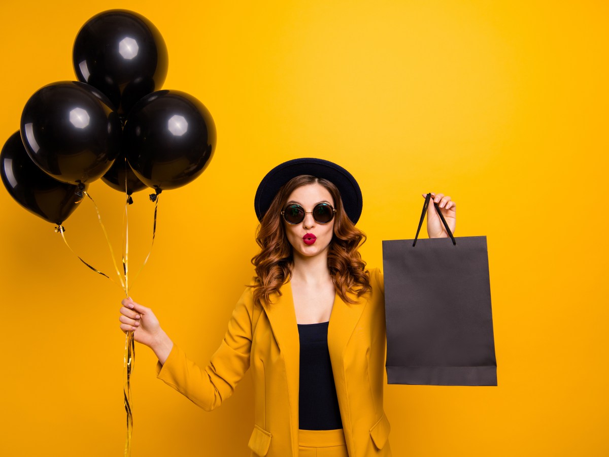 Eine Frau mit braunen Haaren und Sonnenbrille hÃ¤lt schwarze Luftballons und eine schwarze TÃ¼te in der Hand.