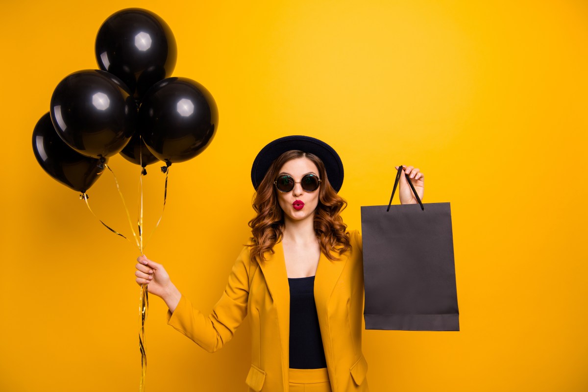 Eine Frau mit braunen Haaren und Sonnenbrille hÃ¤lt schwarze Luftballons und eine schwarze TÃ¼te in der Hand.