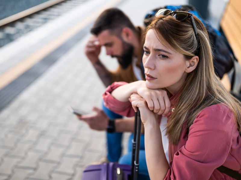 Zwei Reisende sitzen deprimiert am Bahnsteig.