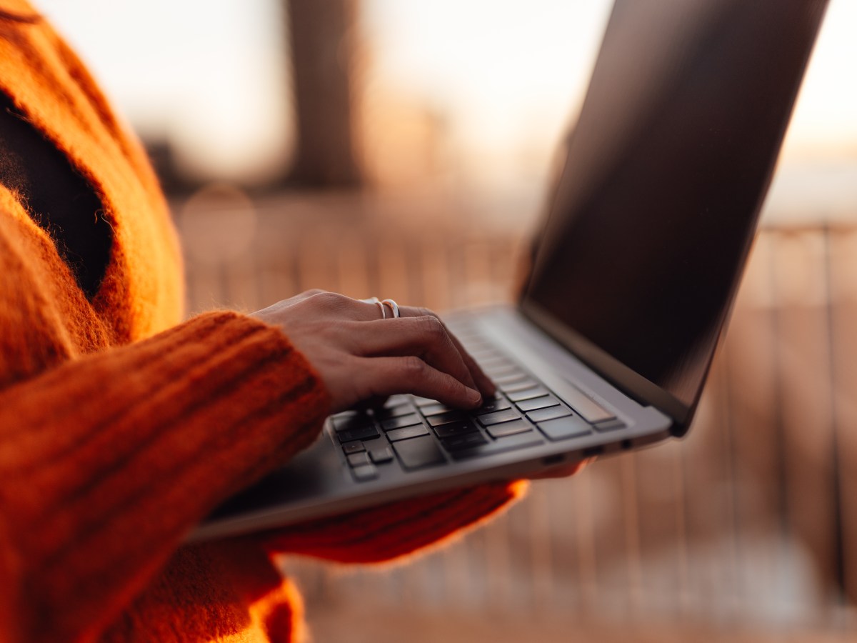 Frau tippt mit der Hand auf einer Laptop-Tastatur in einer AuÃŸenumgebung in der Stadt.