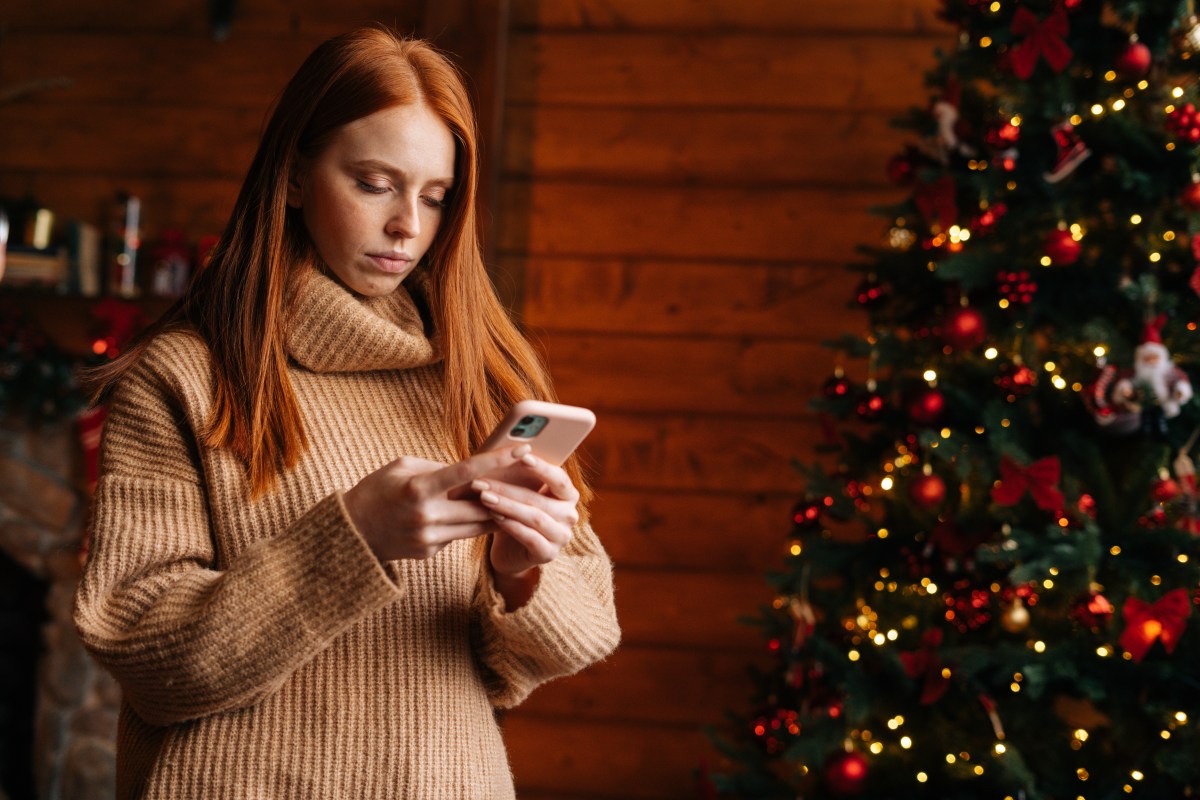 Eine Frau schaut konzentriert auf ihr Handy. Im Hintergrund steht ein Weihnachtsbaum.