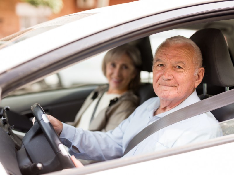 Zwei Senioren sitzen in einem Auto. Der Mann sitzt hinterm Steuer.