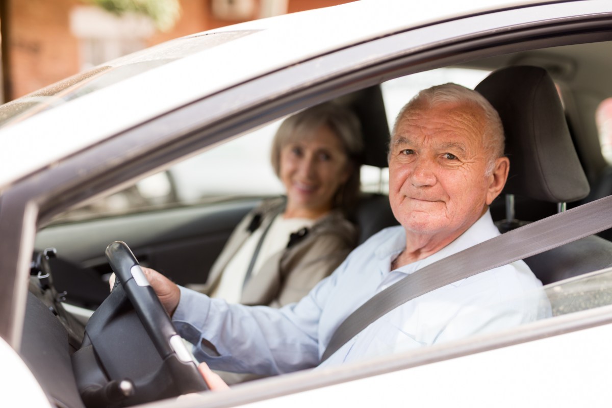 Zwei Senioren sitzen in einem Auto. Der Mann sitzt hinterm Steuer.