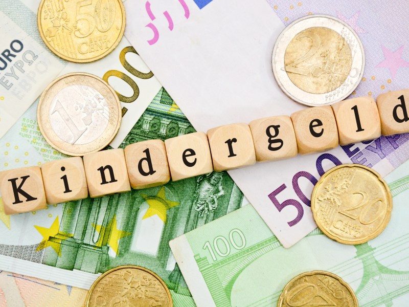 Würfel mit Buchstaben ergeben das Wort "Kindergeld". Sie liegen auf Geldscheinen.