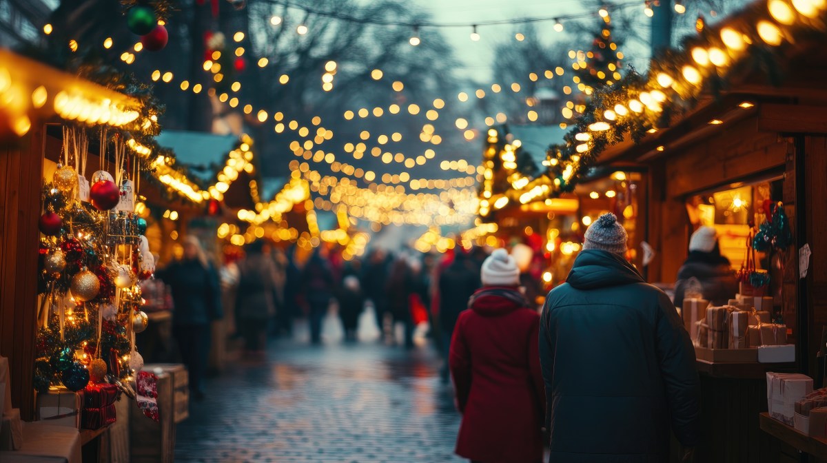 Ein Weihnachtsmarkt am Abend. Die Lichterketten leuchten.