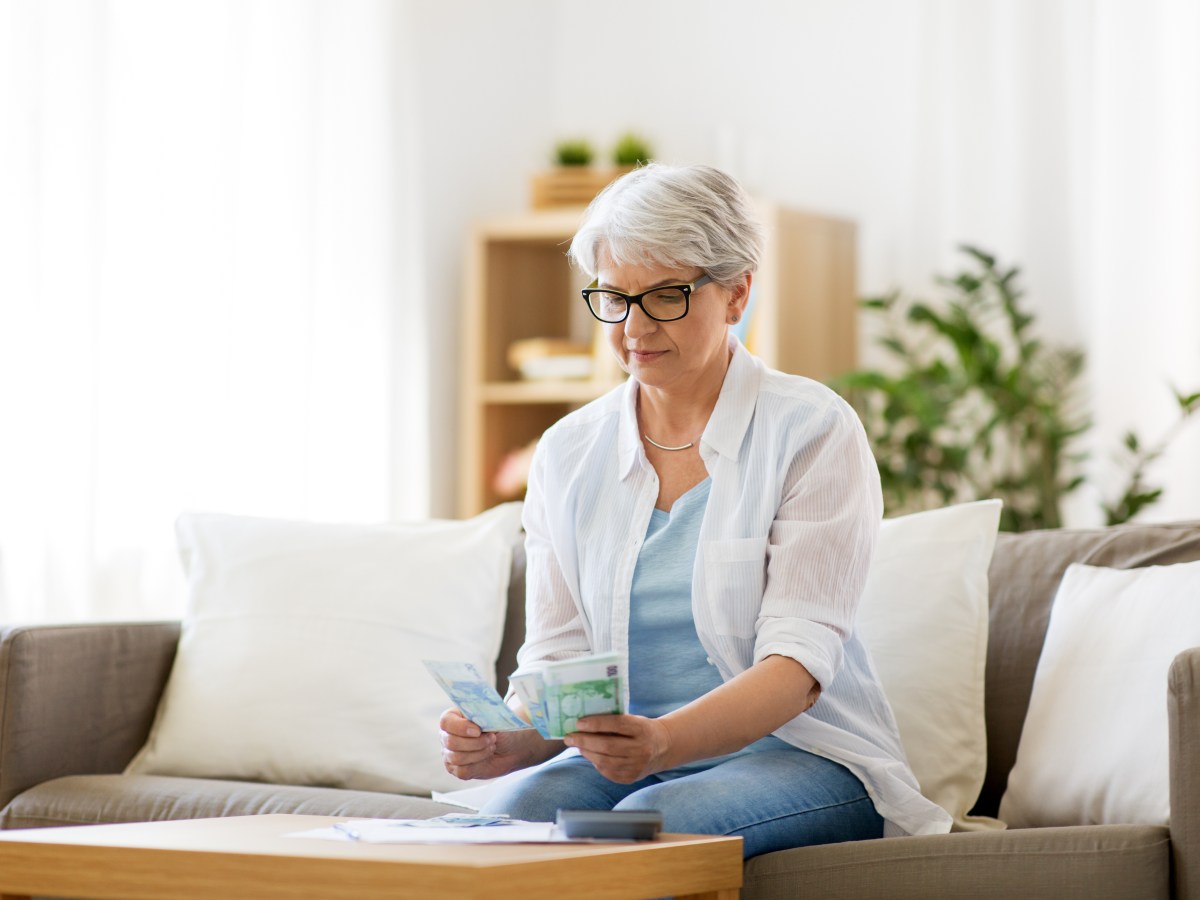 Eine Seniorin sitzt auf der Couch und hÃ¤lt Geld in der Hand.