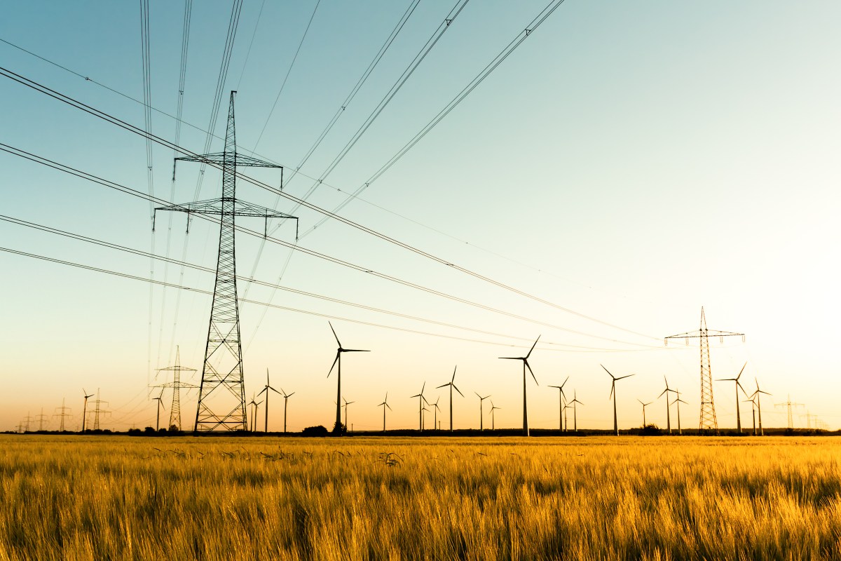 Strommasten im Kornfeld und WindrÃ¤der im Sonnenuntergang.