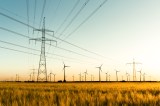 Strommasten im Kornfeld und Windräder im Sonnenuntergang.