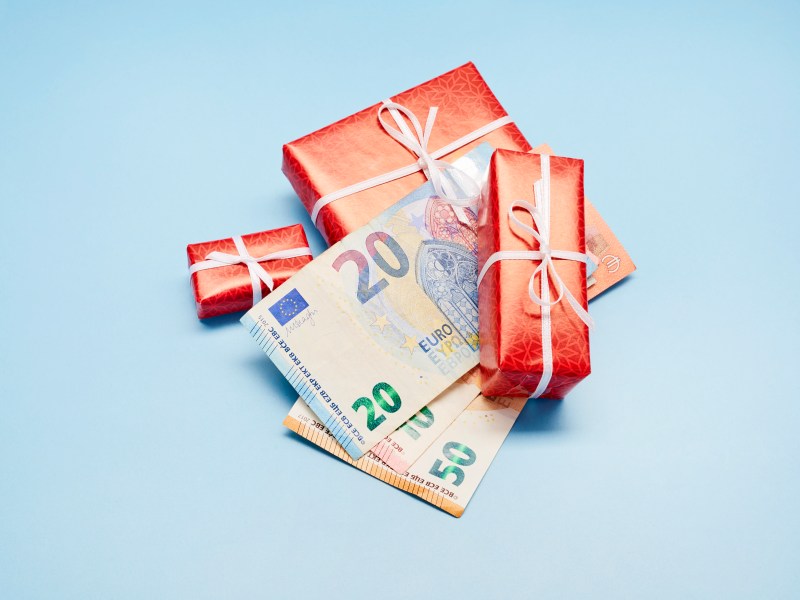 Draufsicht auf verpackte Weihnachtsgeschenke und Euro-Banknoten auf blauem Hintergrund