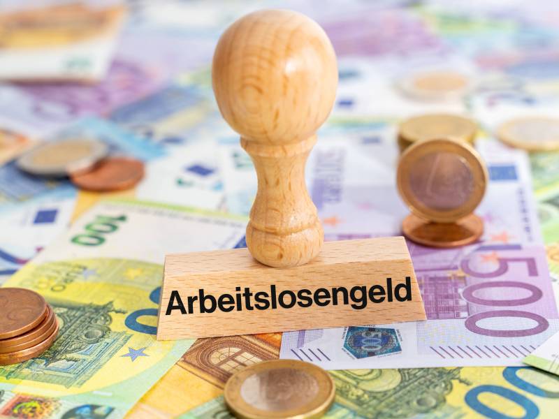 Ein Stempel mit der Aufschrift "Arbeitslosengeld" steht auf Geldscheinen.