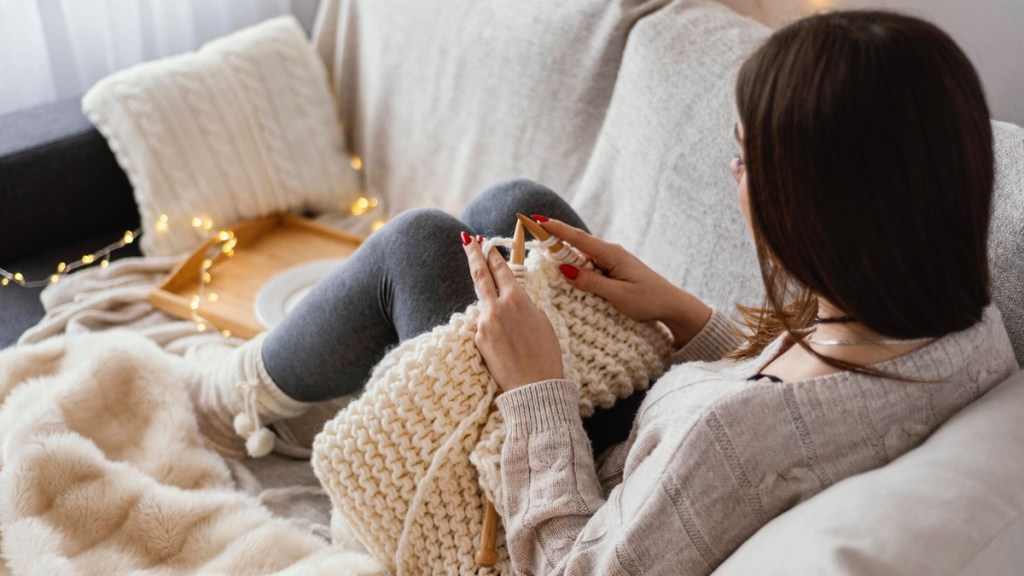 Eine junge Frau liegt auf dem Sofa und strickt.