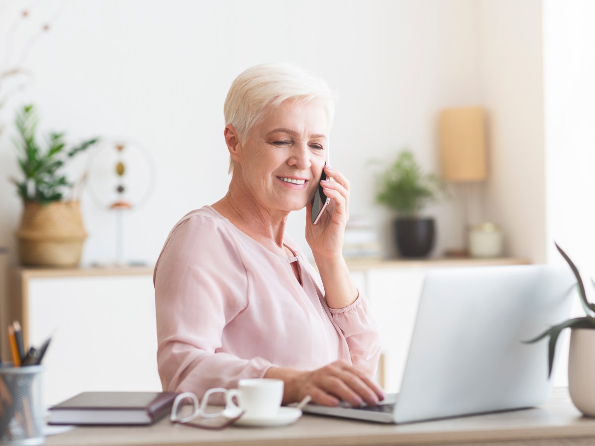 Eine Ã¤ltere Dame sitzt am Laptop und telefoniert.