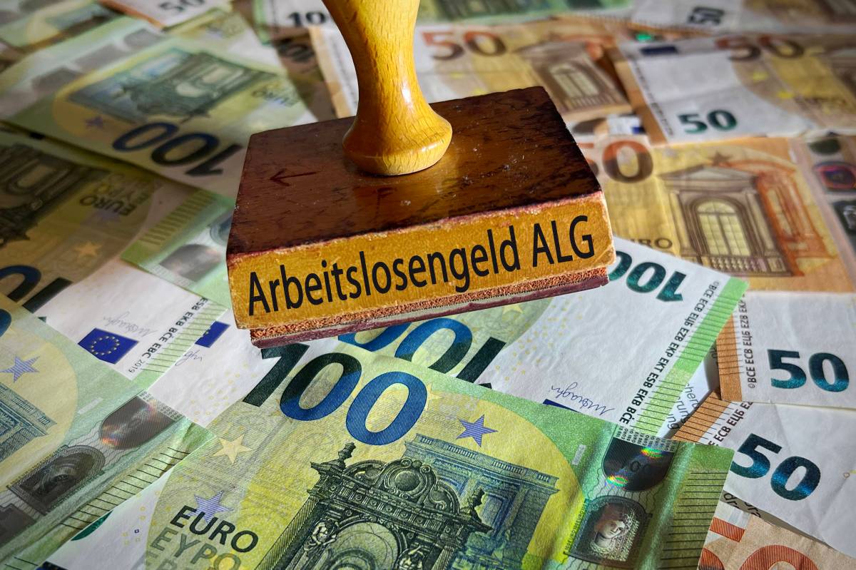 Auf einem Stempel steht das Wort "Arbeitslosengeld ALG". Darunter liegen diverse Geldscheine.