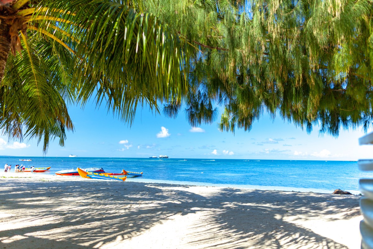 Ein weiÃŸer Sandstrand mit Palmen und blauem Wasser.