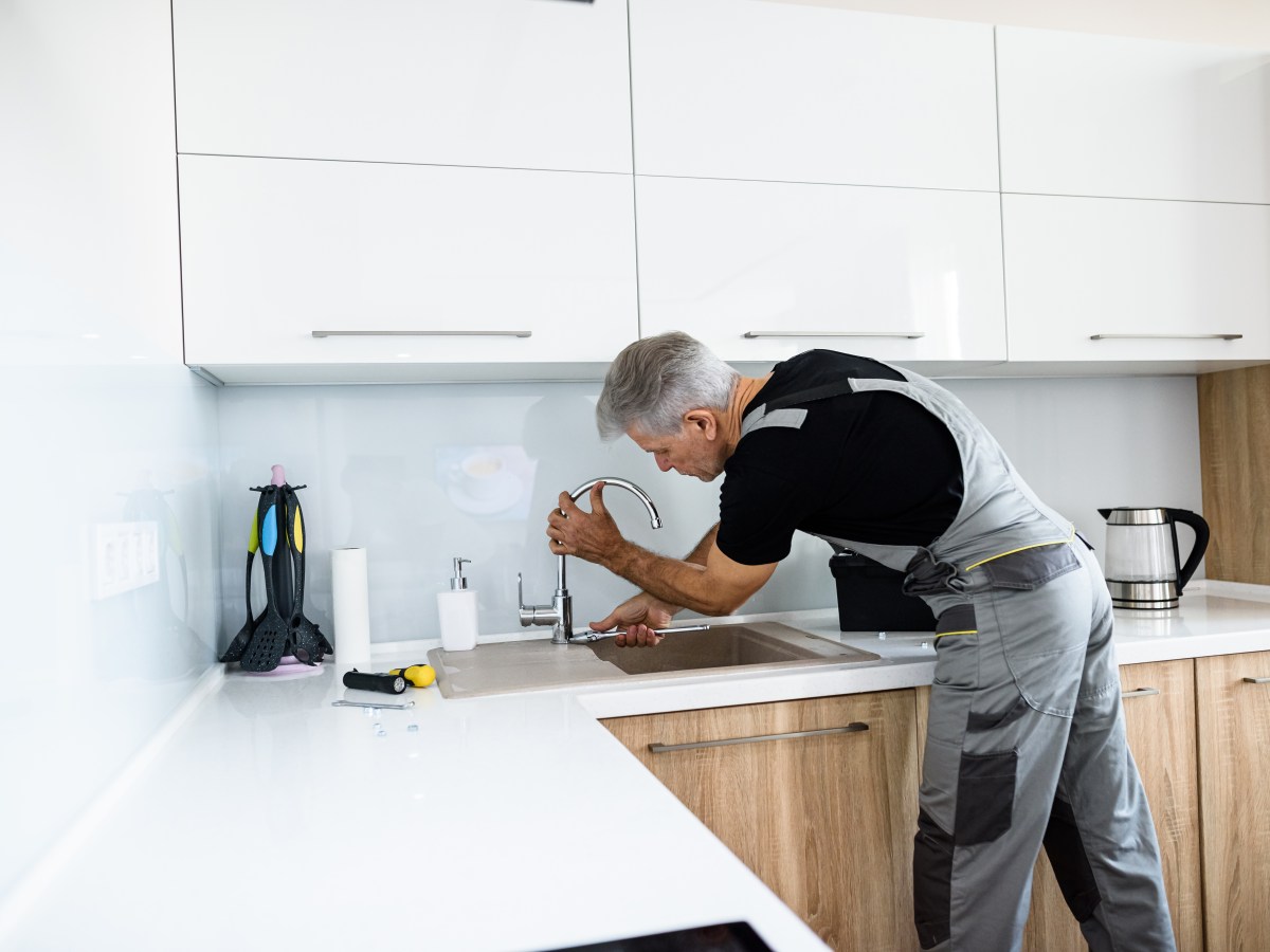 Ein Handwerker steht in der KÃ¼che und repariert den Wasserhahn.