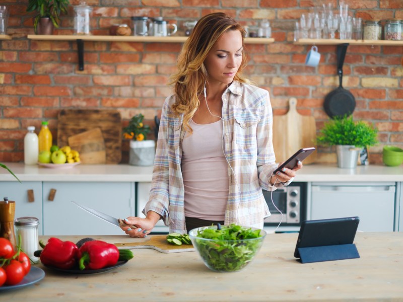 Frau mit Handy-App in der Küchen am Kochen: Hobbys und Side Hustle Ideen für das Sternzeichen Wassermann