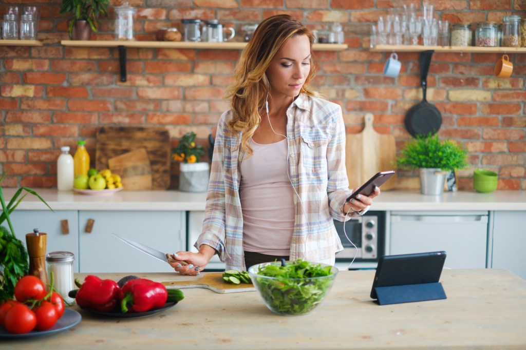 Frau mit Handy-App in der Küchen am Kochen: Hobbys und Side Hustle Ideen für das Sternzeichen Wassermann