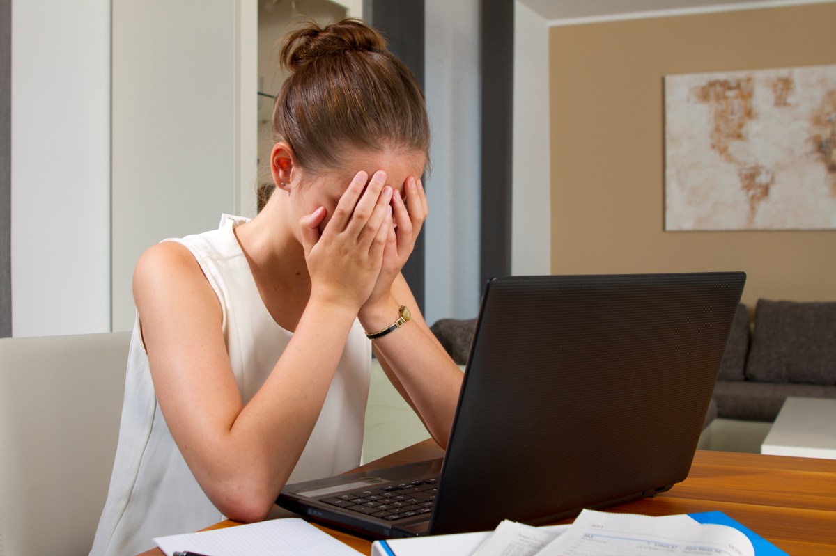 Eine Frau sitzt vor ihrem Laptop und hält die Hände vor ihre Augen.